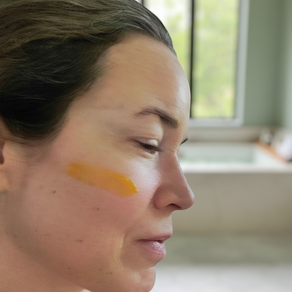 Vital Acre Farm & Apothecary Pure Gold tallow face butter applied as a golden streak on a woman's cheek for hydration.