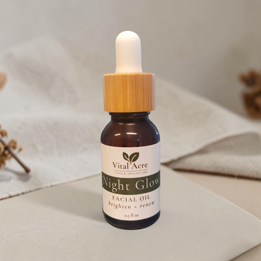 Vital Acre Farm & Apothecary Night Glow facial oil in a brown glass dropper bottle with a wooden cap on a stone surface