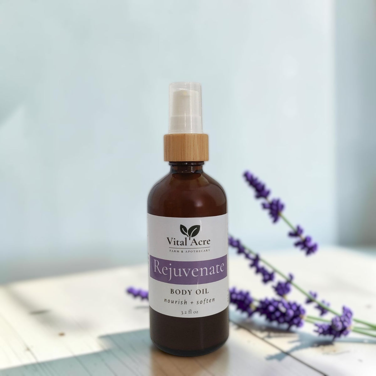 Vital Acre Farm & Apothecary REjuvenate body oil in an amber glass bottle with lavender sprigs on a white surface.