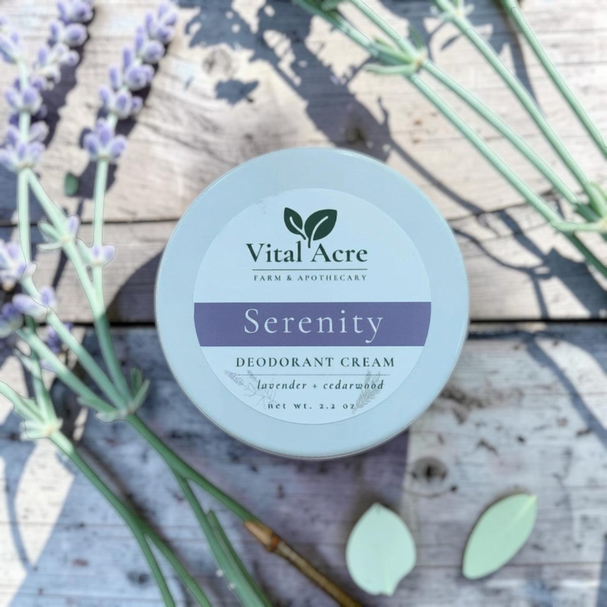 Vital Acre Farm & Apothecary Serenity deodorant cream in a round tin with lavender sprigs on a rustic wooden surface.