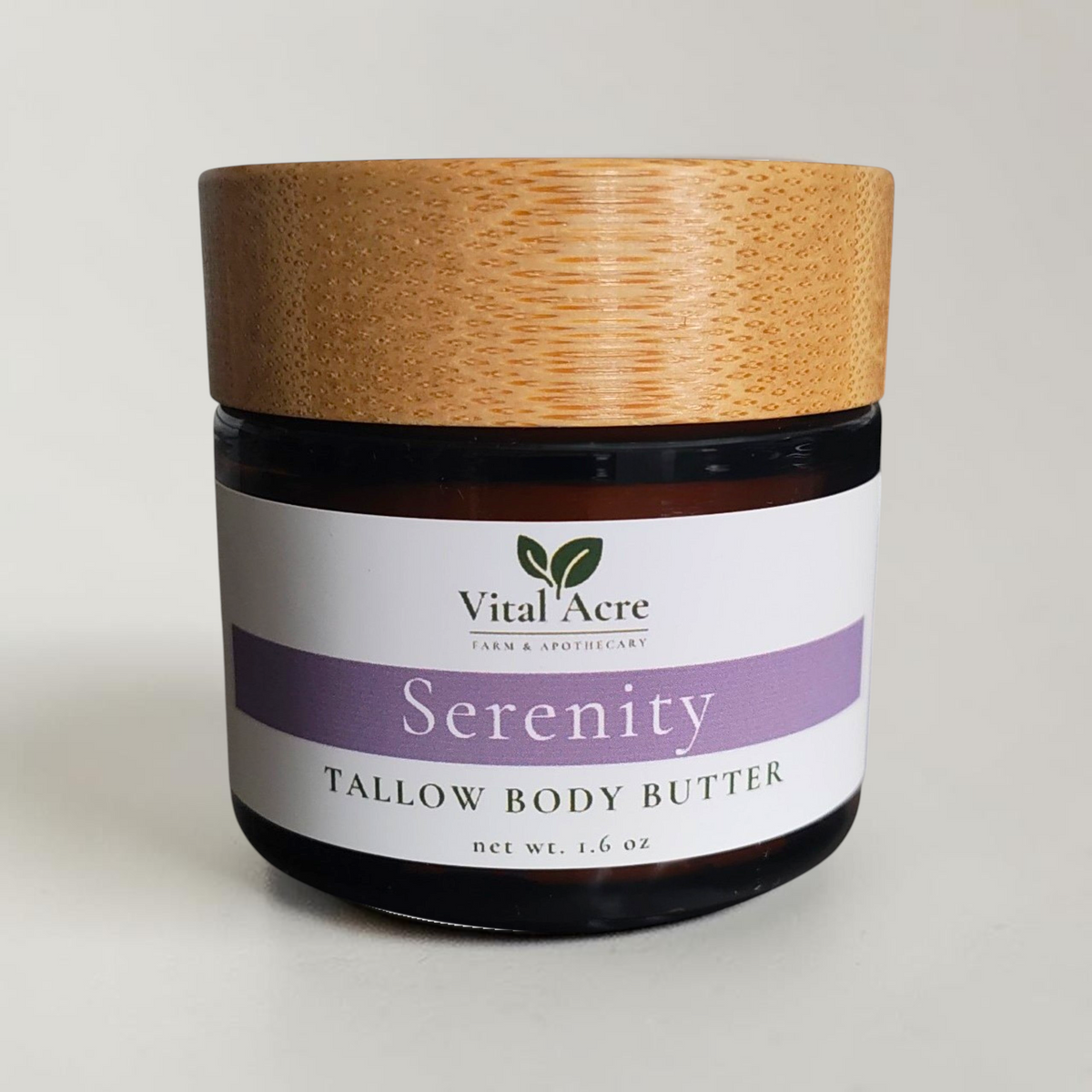 Vital Acre Farm & Apothecary Serenity tallow body butter in an amber glass jar with a wooden lid on a grey surface.
