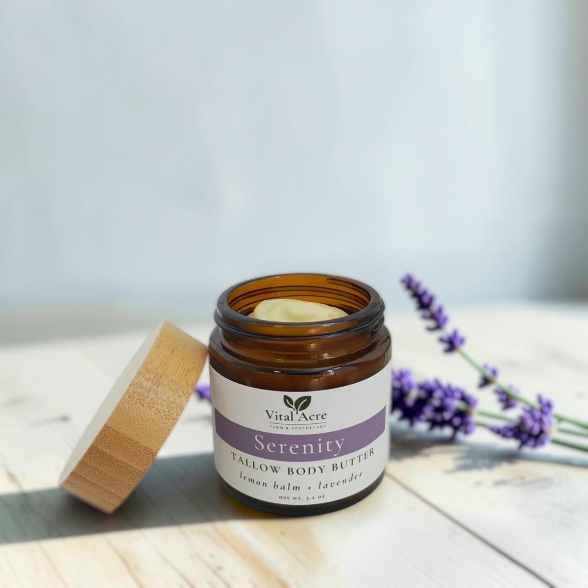 Vital Acre Farm & Apothecary Serenity tallow body butter in an amber glass jar with bamboo lid and lavender sprigs.